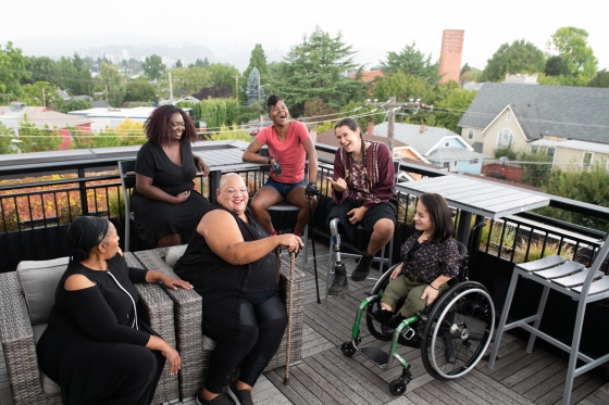 Overhead shot of six disabled people of colour at a rooftop deck party - Disabled and Here