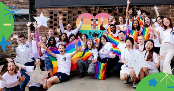 Group photo of UNSW staff and students at a Mardi Gras parade rehearsal holding up stars and rainbow flags
