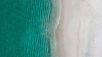 Stock photo of calm, green waves washing up a white, sandy beach