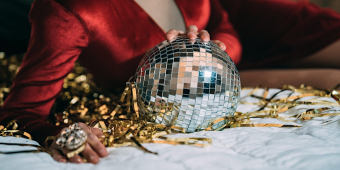 Photo of a person wearing a red dress with one hand on a silver disco ball attached to gold ribbons