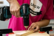 Someone drilling wood wearing a pink t'shirt with UNSW Making on it