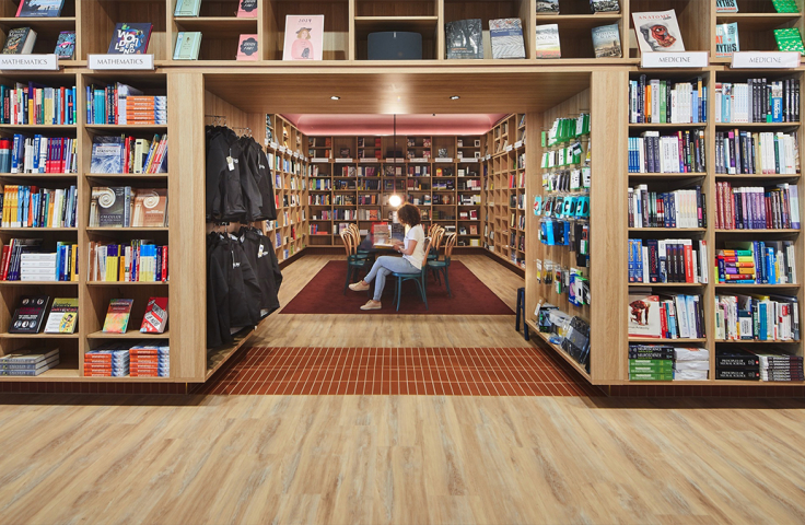 a person sat a table in middle with tall wooden shelfs surrounding them in a bookshop rary