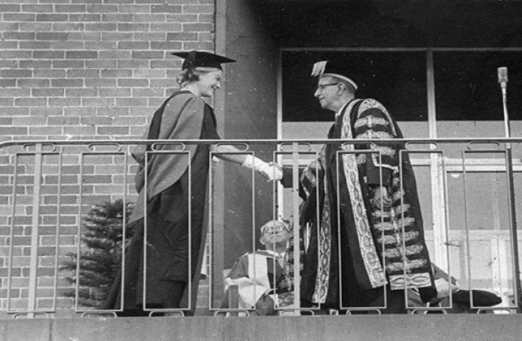 A female student graduate shakes the hand of a male University Professor. 