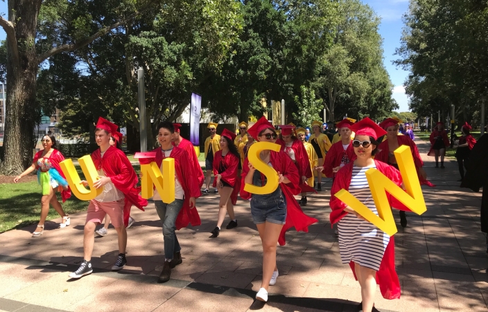 People dressed in red and yellow robes carry letters spelling UNSW