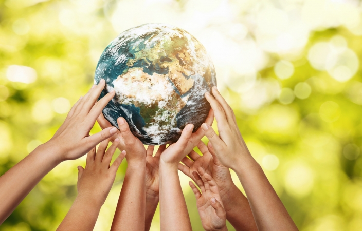 a few sets of hands holding a globe up  in the air against a green forest background