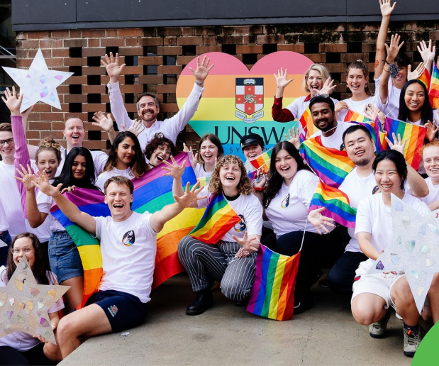 Group photo of UNSW staff and students at a Mardi Gras parade rehearsal holding up stars and rainbow flags