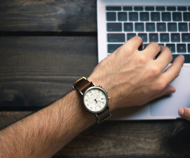 Man looking at a wrist watch while on a laptop