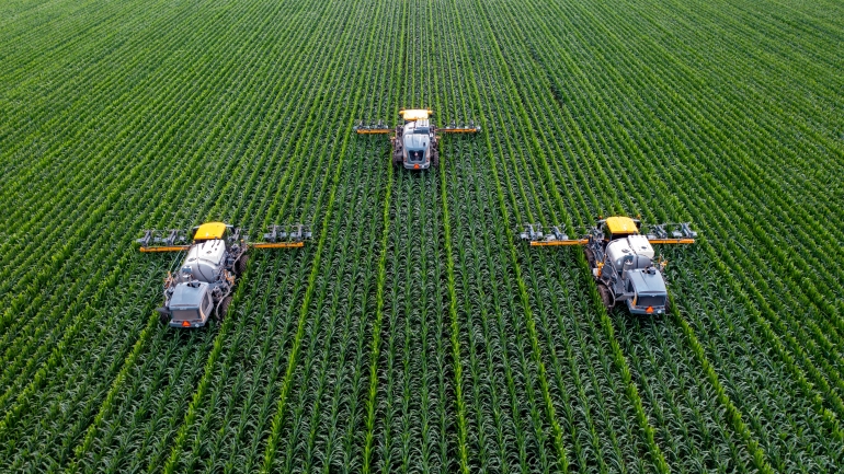 3 large machines farming a green field of crops
