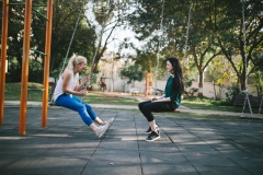 2 girls facing each other, swinging on swings