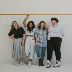 4 women laughing against a wall