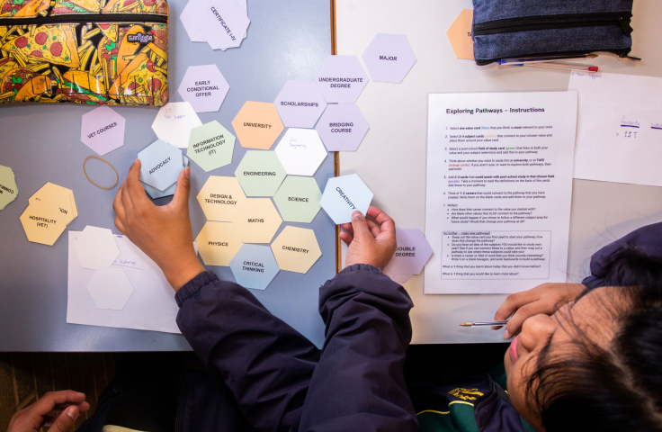 overhead view of hexagons on a table with words on them and a young student looking to connect them together 