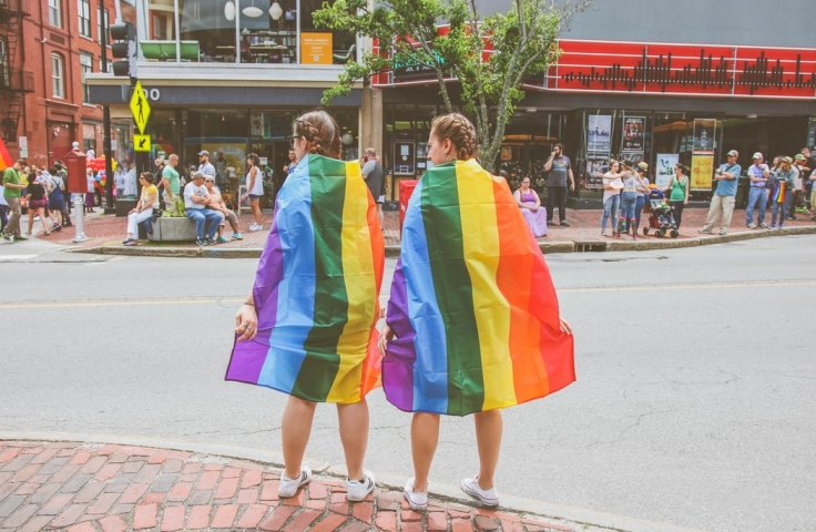 Two people draped in rainbow flags. 