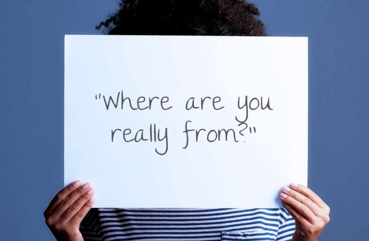 A person holds a sign that reads "Where are you really from?"