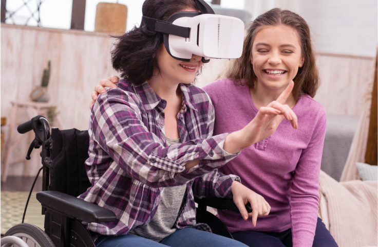 2 young women experimenting with VR. The one with a headset on is in a wheelchair and the other is sat next to her