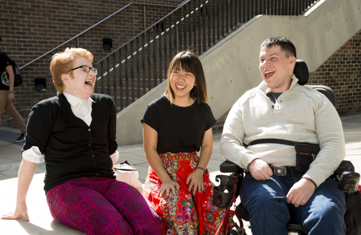 Photo of three students smiling and laughing, one student is a wheelchair user