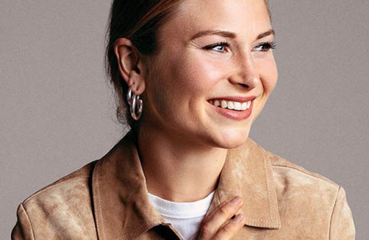 Grace Tame smiling and looking to her left, with her hair tied up and wearing a camel coloured shirt