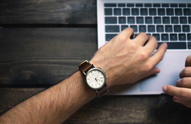 Man looking at a wrist watch while on a laptop