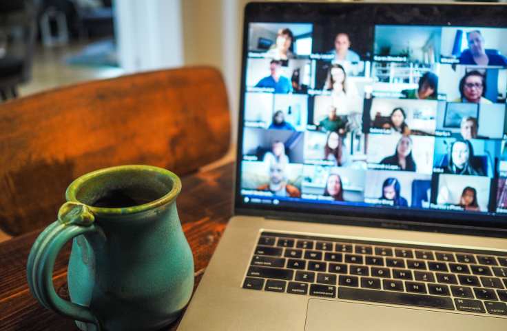 A big mug on a desk next to a laptop showing lots of people on a webinar