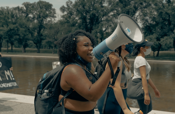 Black woman walking and talking in to a megaphone
