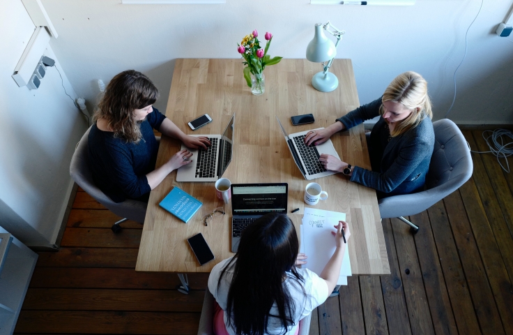 overhead view of 3 women working at a table on laptops