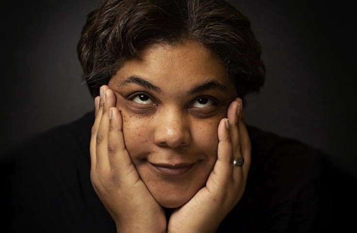 Roxane Gay posing with her chin in her hands, smiling and looking up