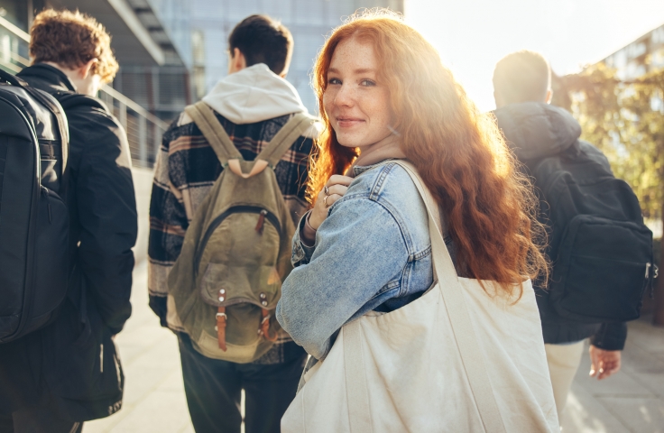 Female red hair student walking behind friends and looking at the camera