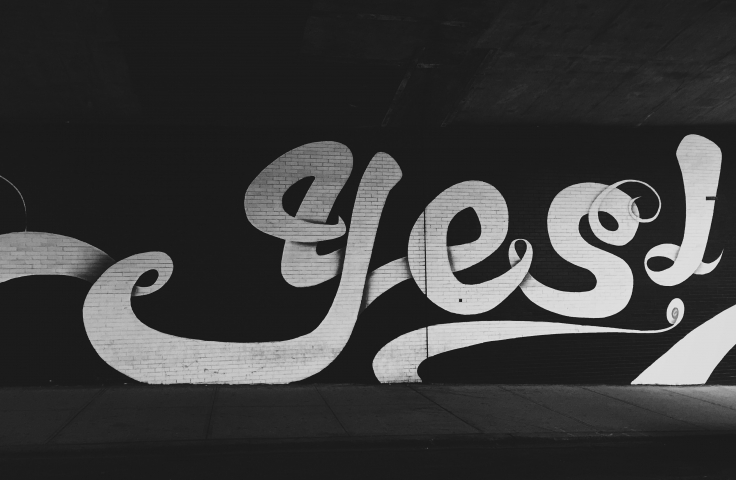 B&W picture of a graffiti brick wall with big white letters saying YES!
