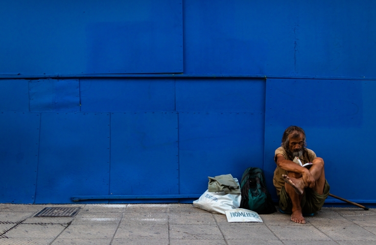 Homeless man sat against a bright blue wall