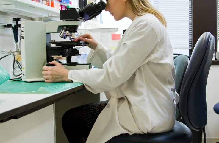 White woman in lab coat looking at a microscope
